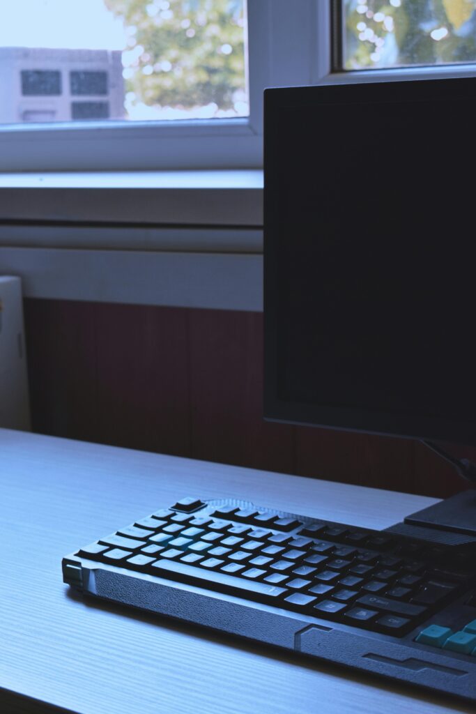 Minimalist workspace featuring a sleek keyboard and monitor by a window.